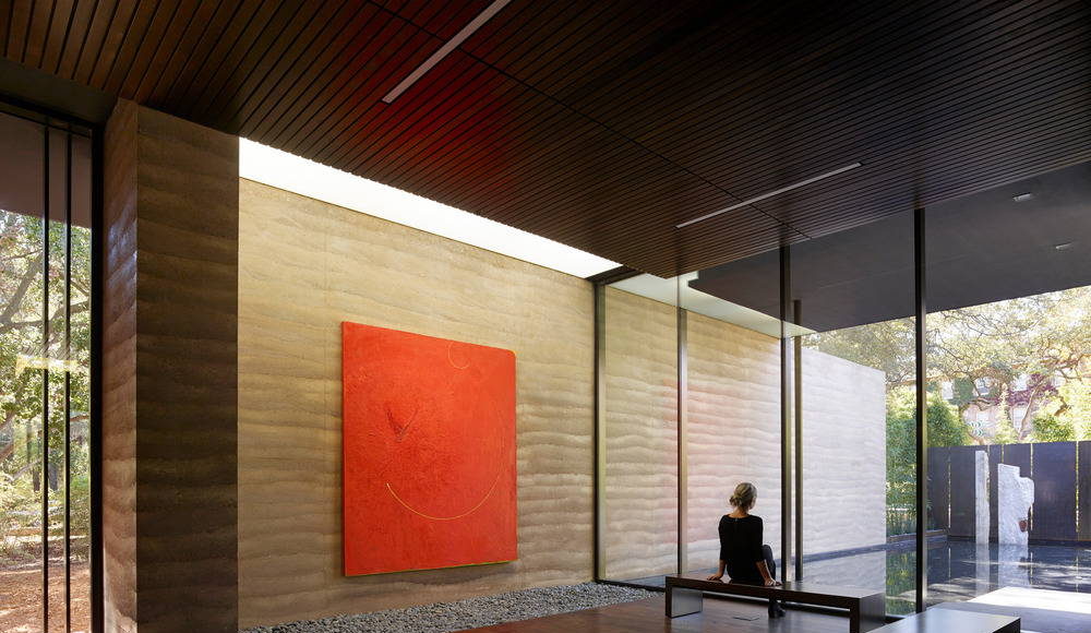 Nathan Oliveira’s “Big Red” greets visitors upon entering the building. The rammed earth wall extends from the entry to the reflecting pool beyond, blurring the line between interior and exterior : Photo credit © Matthew Millman