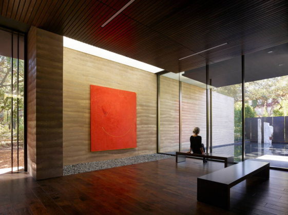 Nathan Oliveira’s “Big Red” greets visitors upon entering the building. The rammed earth wall extends from the entry to the reflecting pool beyond, blurring the line between interior and exterior : Photo credit © Matthew Millman