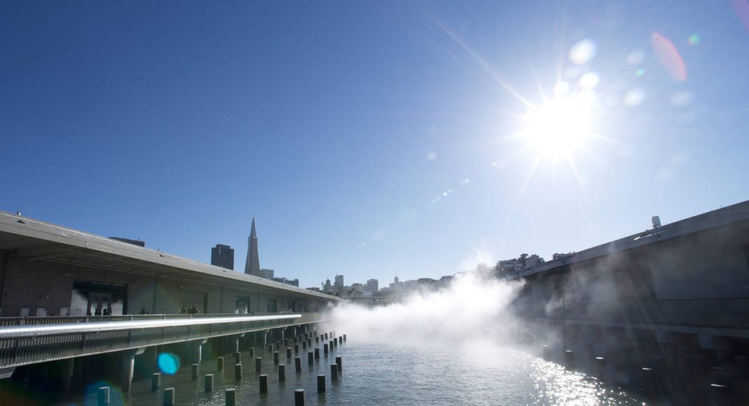 Vista hacia la ciudad entre los Muelles 15 y 17. La exposición de otro mundo Fog Bridge creada por el artista Fujiko Nakaya envuelve al puente conector entre los Muelles 15 y 17 en la distancia. El Exploratorium removió un estacionamiento entre los dos muelles para descubrir el agua. Ahora el agua forma parte del espacio de exhibición presentando obras tales como Color of Water, una exposición montada sobre los pilotes del antiguo muelle que exhorta a los espectadores a descubrir el cambio de colores de la Bahía : Image by Amy Snyder © Exploratorium, www.exploratorium.edu