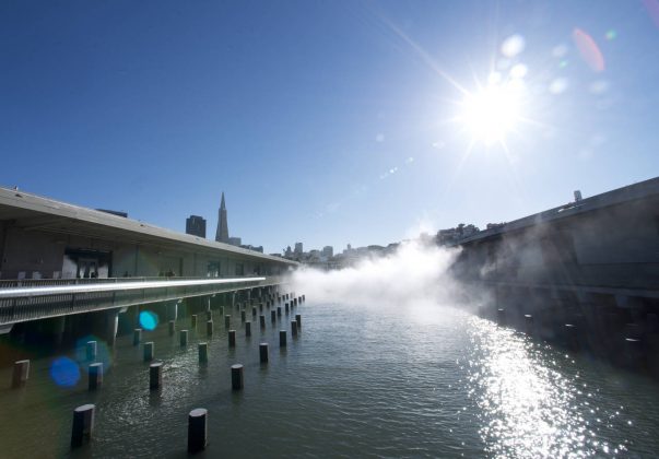 Vista hacia la ciudad entre los Muelles 15 y 17. La exposición de otro mundo Fog Bridge creada por el artista Fujiko Nakaya envuelve al puente conector entre los Muelles 15 y 17 en la distancia. El Exploratorium removió un estacionamiento entre los dos muelles para descubrir el agua. Ahora el agua forma parte del espacio de exhibición presentando obras tales como Color of Water, una exposición montada sobre los pilotes del antiguo muelle que exhorta a los espectadores a descubrir el cambio de colores de la Bahía : Image by Amy Snyder © Exploratorium, www.exploratorium.edu