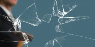 Business Man with Sledgehammer behind a broken Glass Pane vía Shutterstock