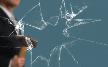 Business Man with Sledgehammer behind a broken Glass Pane vía Shutterstock