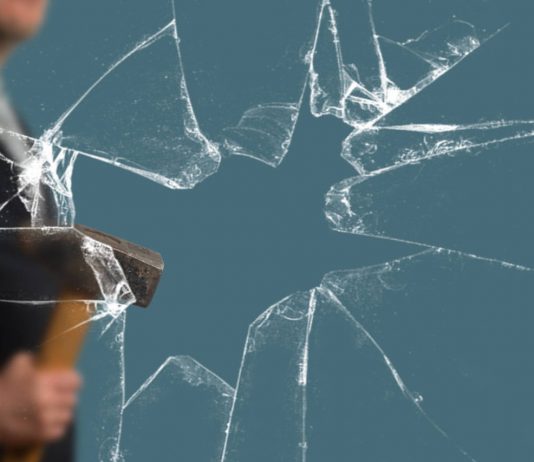 Business Man with Sledgehammer behind a broken Glass Pane vía Shutterstock