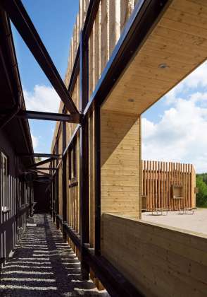 The screen of timber wraps around the building with openings for entry and extra sunlight intake. Protruding wooden boxes also provides space for benches, signage and artwork : Photo credit © Åke E:son Lindman