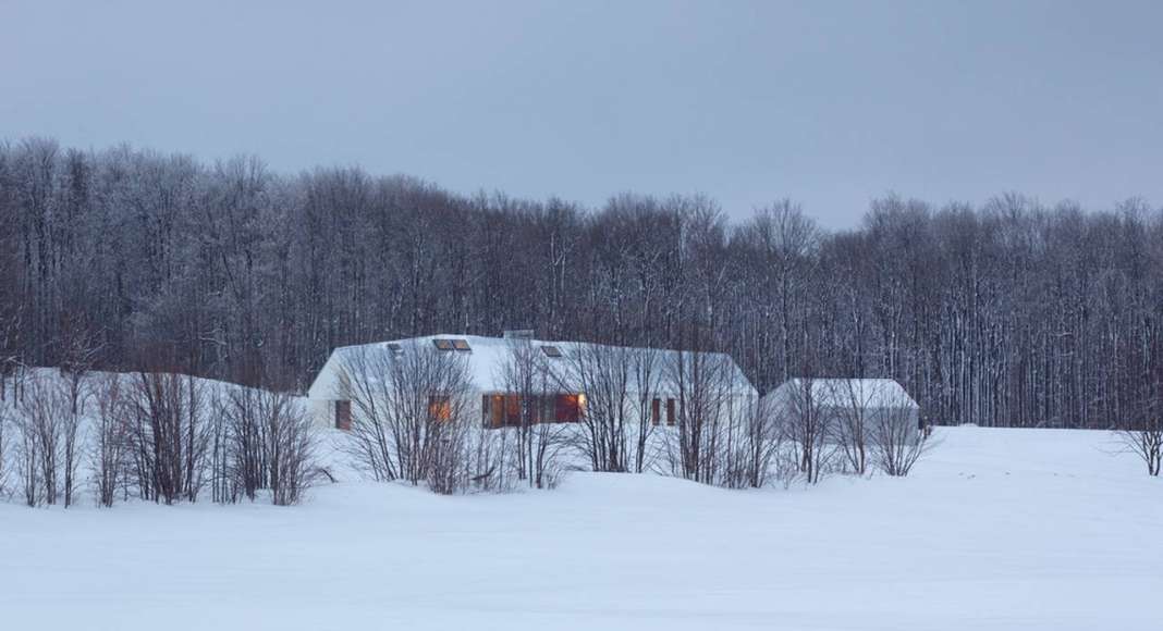 Set back into the 200-acre property and away from the road, the house is nestled into the land and against a line of trees that act as a windbreak and provide a sense of enclosure. The house virtually disappears into the snowy whiteness of the winter landscape : Photo credit © Ben Rahn / A-Frame Studio