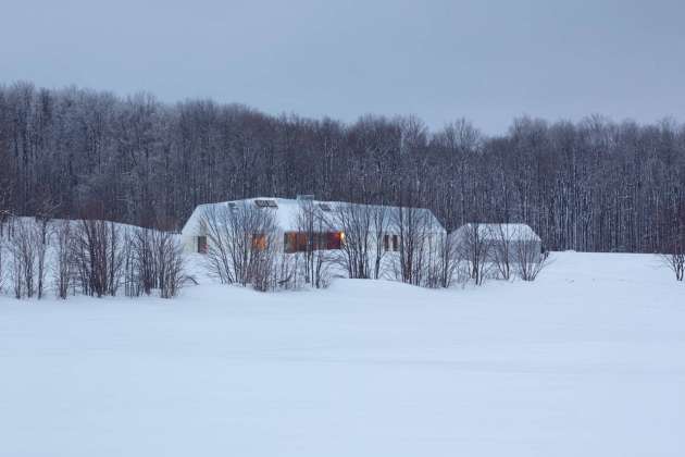 Set back into the 200-acre property and away from the road, the house is nestled into the land and against a line of trees that act as a windbreak and provide a sense of enclosure. The house virtually disappears into the snowy whiteness of the winter landscape : Photo credit © Ben Rahn / A-Frame Studio