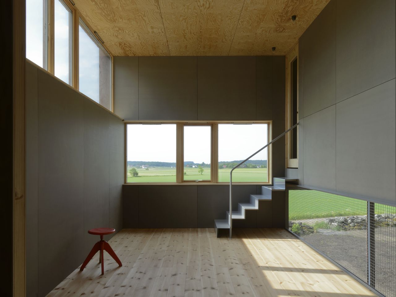 Second floor living room with its offset slab and transparency. A rolled powder coated sheet staircase leads to the building's highest placed space. The highest placed window dipped down diagonally throughout the entire building. : Photo © Bornstein Lyckefors Arkitekter